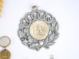 a gold coin sitting on top of a silver broochle