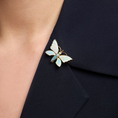 a close up of a woman wearing a gold and white butterfly broochle
