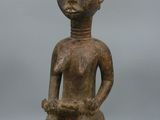 une vieille statue en bois représentant un homme assis sur un tabouret