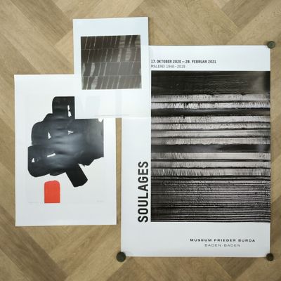 trois affiches en noir et blanc posées sur un plancher en bois, avec un objet rouge
