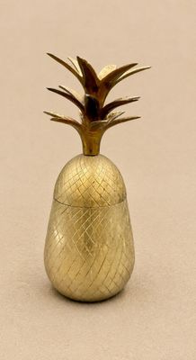 un récipient doré en forme d'ananas posé sur une surface beige