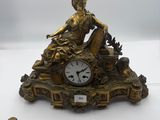 a gold clock with a woman sitting on it