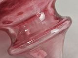 a pink glass vase with a curved handle on a table