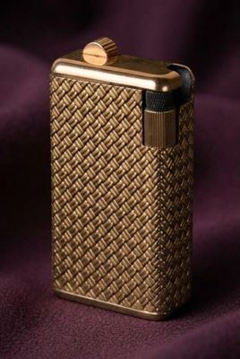 un gros plan d'un briquet doré posé sur un tissu violet