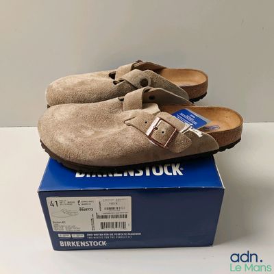une paire de sabots en daim marron posée sur une boîte bleue