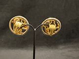 pair of gold plated earrings on a black stand against a black background