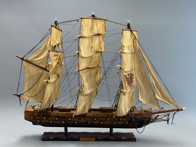 maquette en bois d'un voilier posée sur un socle, sur fond gris