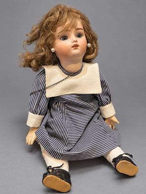 an old doll sitting on the ground wearing a blue and white striped dress
