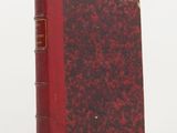 an old book with a red cover sitting on top of a white table