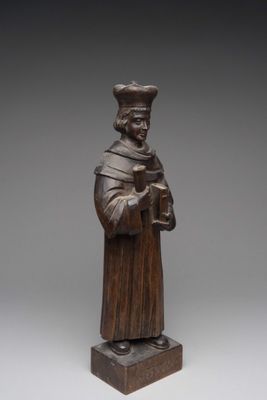 a wooden statue of a man holding a book and wearing a hat