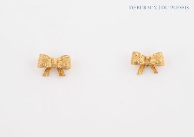 deux petites boucles d'oreilles en forme de nœud dorées posées sur un fond blanc