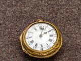 une petite horloge en or avec des chiffres romains