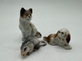 three figurines of cats and a dog on a white surface
