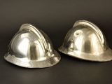 pair of silver plated hard hats on a black background