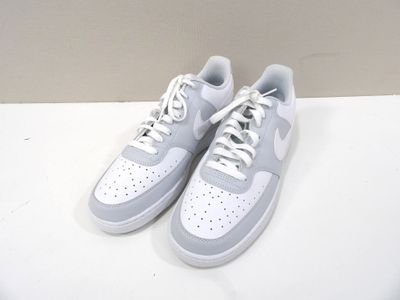 une paire de baskets blanches et grises posées sur une surface blanche, avec un mur en arrière-plan