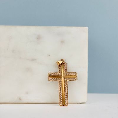 une croix en or posée sur un bloc de marbre blanc, sur fond bleu