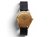 une montre en or avec un bracelet noir posée sur une surface blanche