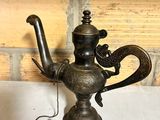 a small metal teapot sitting on a table next to a brick wall