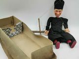 a doll that is sitting next to a cardboard boat