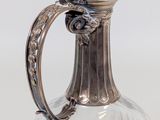 a glass pitcher with a metal handle on a white surface