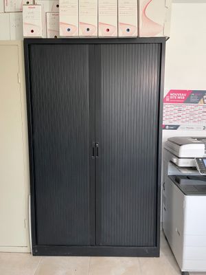 une armoire noire dans un coin de la pièce, avec une imprimante posée dessus