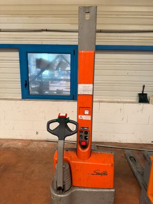 un chariot élévateur orange dans un entrepôt, avec une télévision en arrière-plan