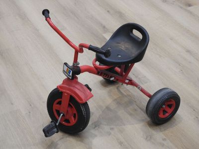 un petit tricycle rouge sur un plancher en bois