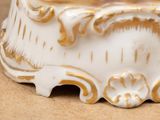 a close up of a white and gold vase on a table