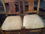 pair of wooden chairs with tan upholstered seats in a warehouse