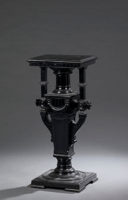 un vase noir ancien posé sur un socle, sur fond gris