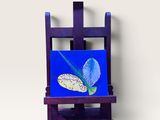 chevalet violet sur lequel est accrochée une peinture représentant une fleur bleue sur fond bleu