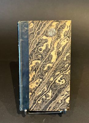 an old book with a black cover sitting on top of a table