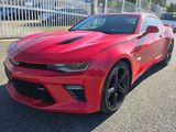La Chevrolet Camaro rouge est garée devant une clôture blanche.