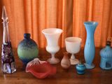 many different vases sitting on a table in front of an orange curtain