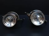 pair of silver plated teapots on a black surface