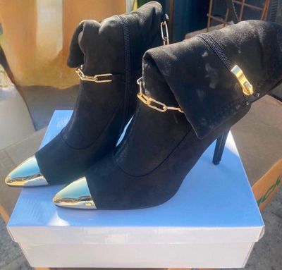 une paire de bottes à talons hauts noires et dorées posées sur une boîte blanche