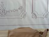 beige leather handbag sitting on a wooden table in front of a white wall