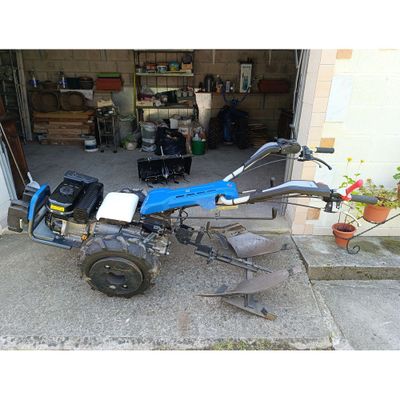 une photo d'un petit tracteur bleu garé devant un garage