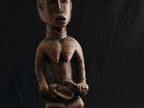 une vieille statue en bois représentant un homme tenant un serpent, sur fond noir