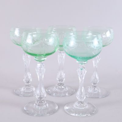 four green wine glasses sitting next to each other on a white surface