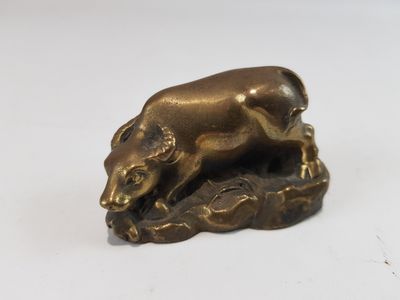 figurine en laiton représentant un taureau posé sur un rocher, sur un fond blanc