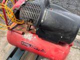 a red air compressor sitting on a pallet next to a bike