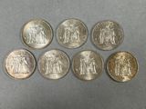 six different coins of different sizes and shapes on a gray surface