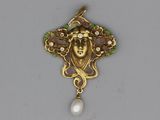 a close up of a pendant with a face and a pearl