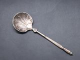 a silver spoon with a shell shaped handle on a black surface