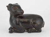 une petite statue représentant un mouton assis sur une surface blanche