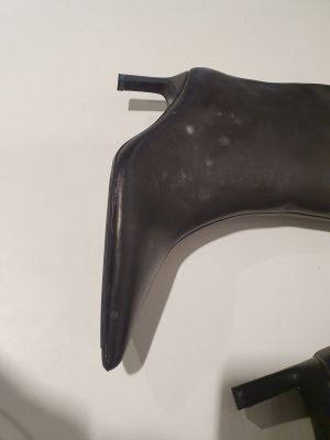des bottes en cuir noir posées sur une table blanche, à côté d'une paire d'escarpins noirs