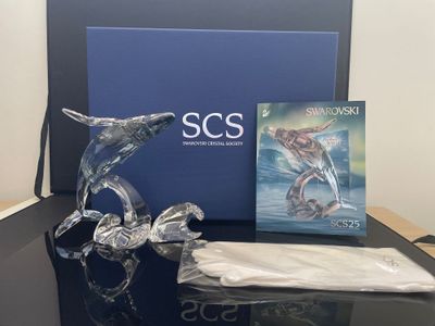 une figurine de dauphin en verre posée sur une table à côté d'un livre