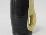 une tasse noire avec une anse jaune posée sur une table blanche