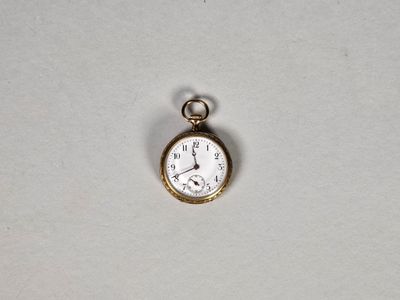 une petite montre de poche en or posée sur une surface blanche